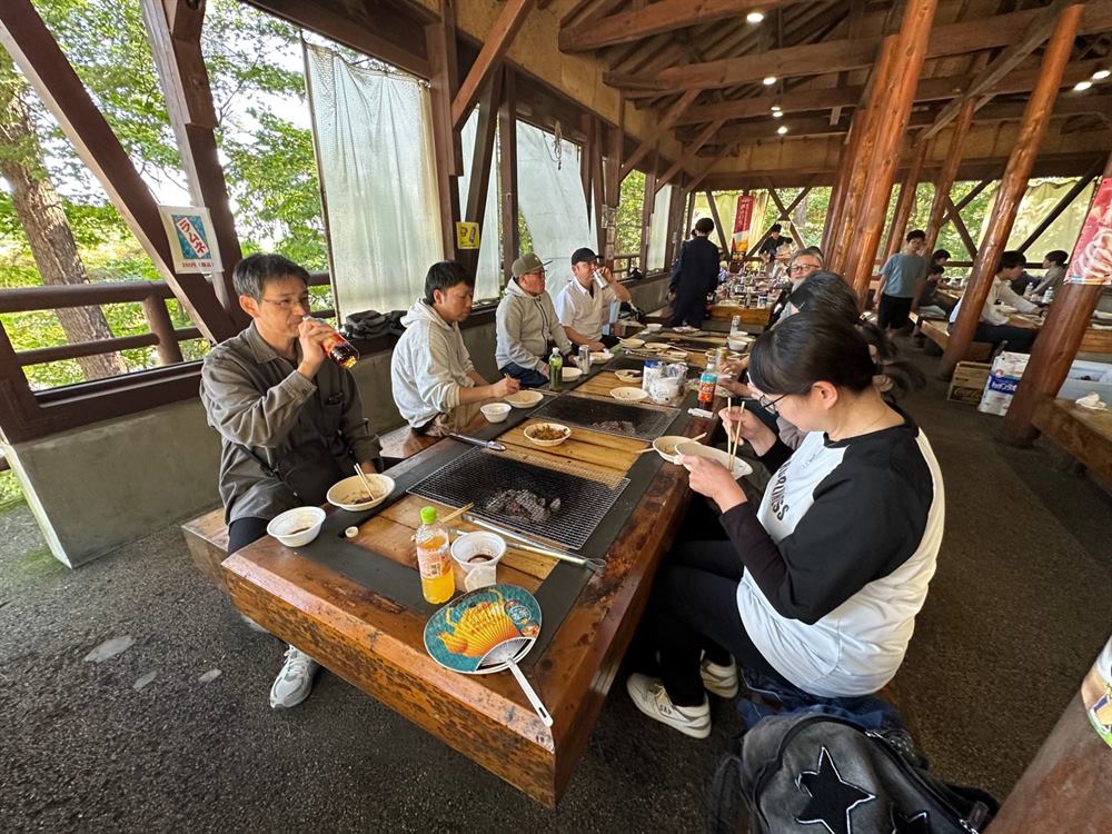 木組みの屋根の下、炭火の卓を囲んでバーベキューを楽しむ人たち