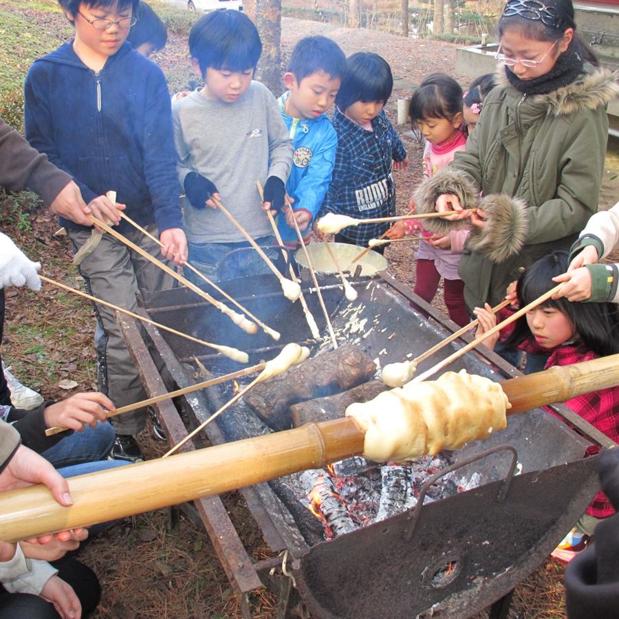 炭火の上で竹に生地を巻きつけてバウムクーヘンを焼く子どもたち