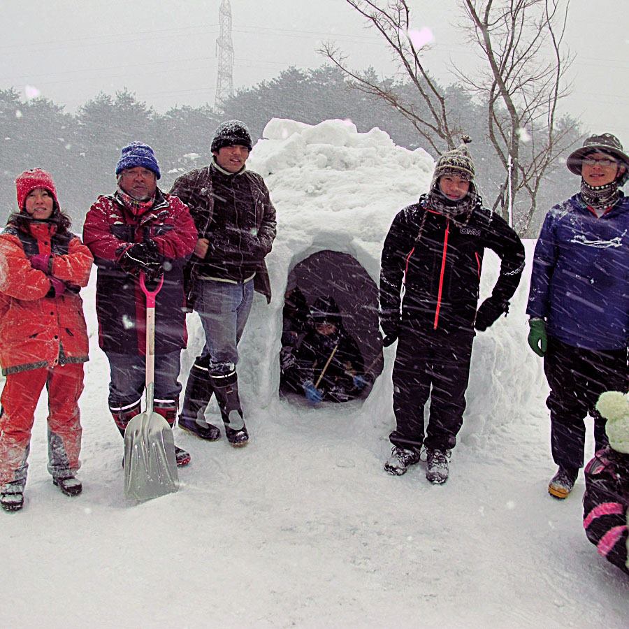 雪の中に作ったイグルーの前に並ぶ参加者たち